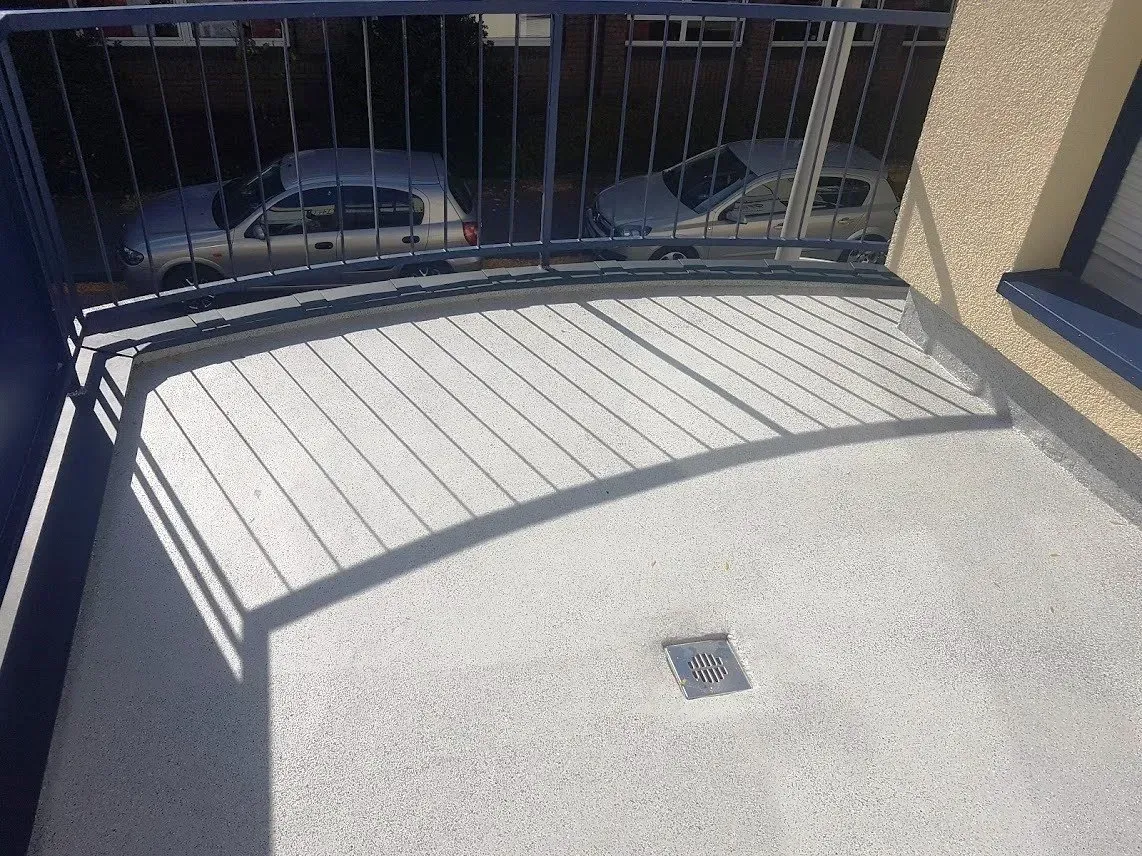 Geschwungene, weiße Terrassenfläche mit schwarzem Geländer, das Schatten wirft, mit Blick auf die darunter geparkten Autos.