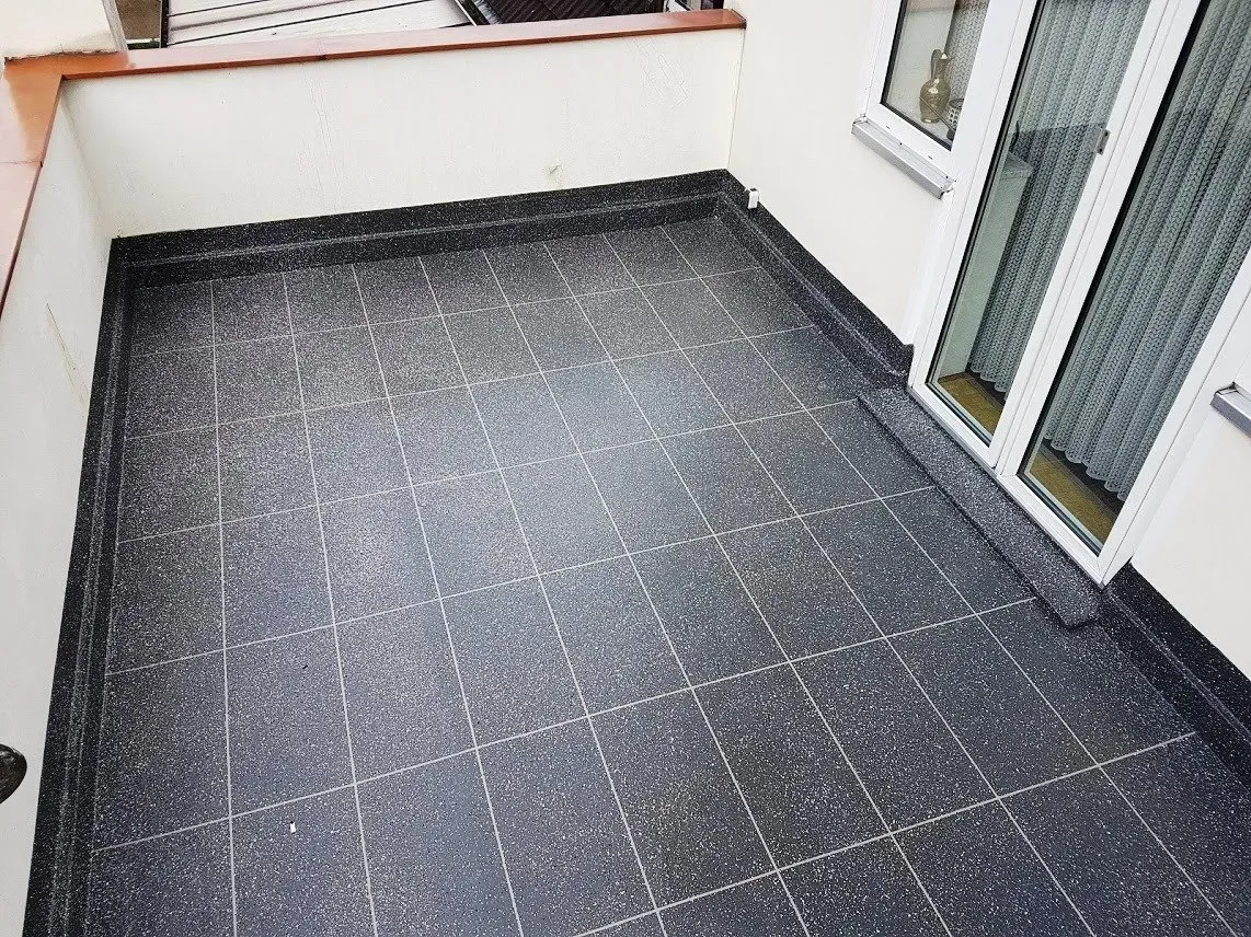 Kleiner gefliester Balkon mit dunklem Boden, weißen Wänden und Glasschiebetüren.