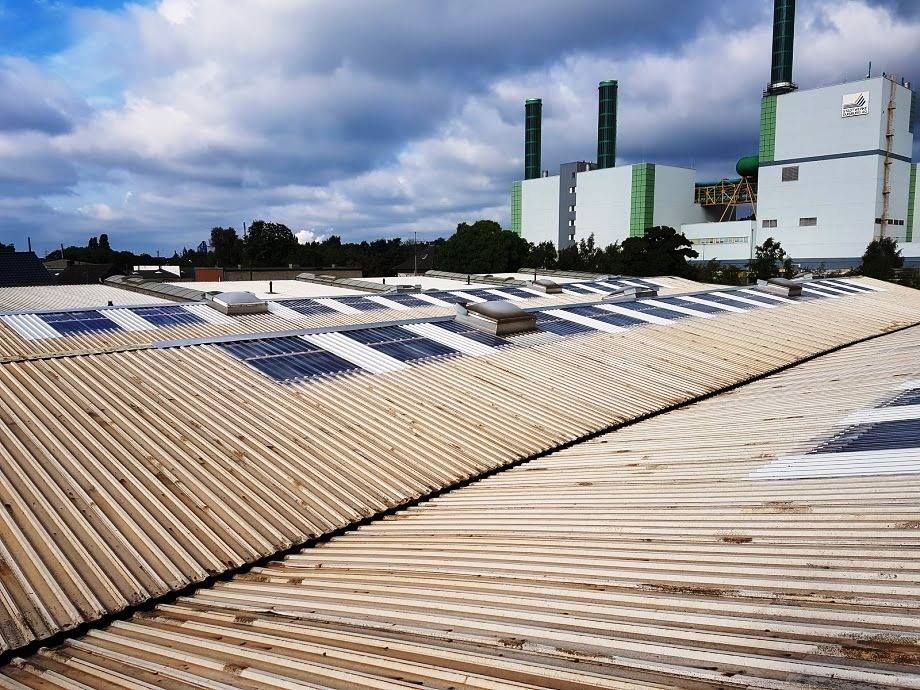 Industriedach mit Reihen schräg angeordneter Solarpaneele unter einem bewölkten Himmel