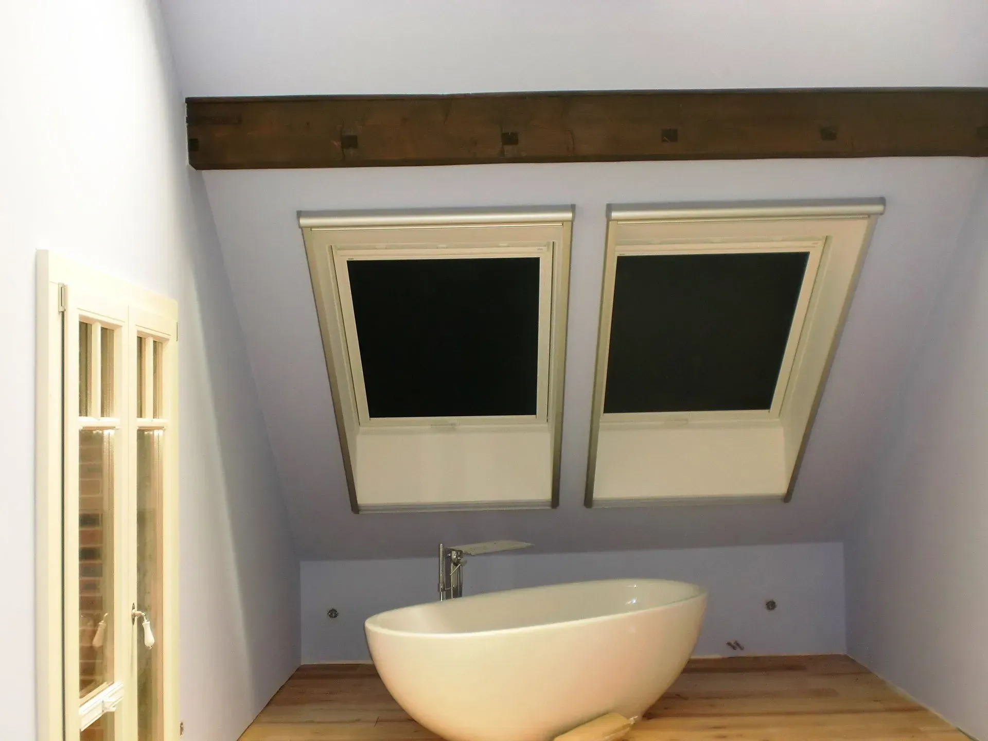 Kleines Dachgeschossbad mit Waschbecken und zwei Dachfenstern über einer schrägen Wand.