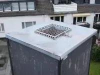 Dachlüftungsanlage mit quadratischem Metallgitter auf einem flachen grauen Dach in der Nähe von Gebäuden