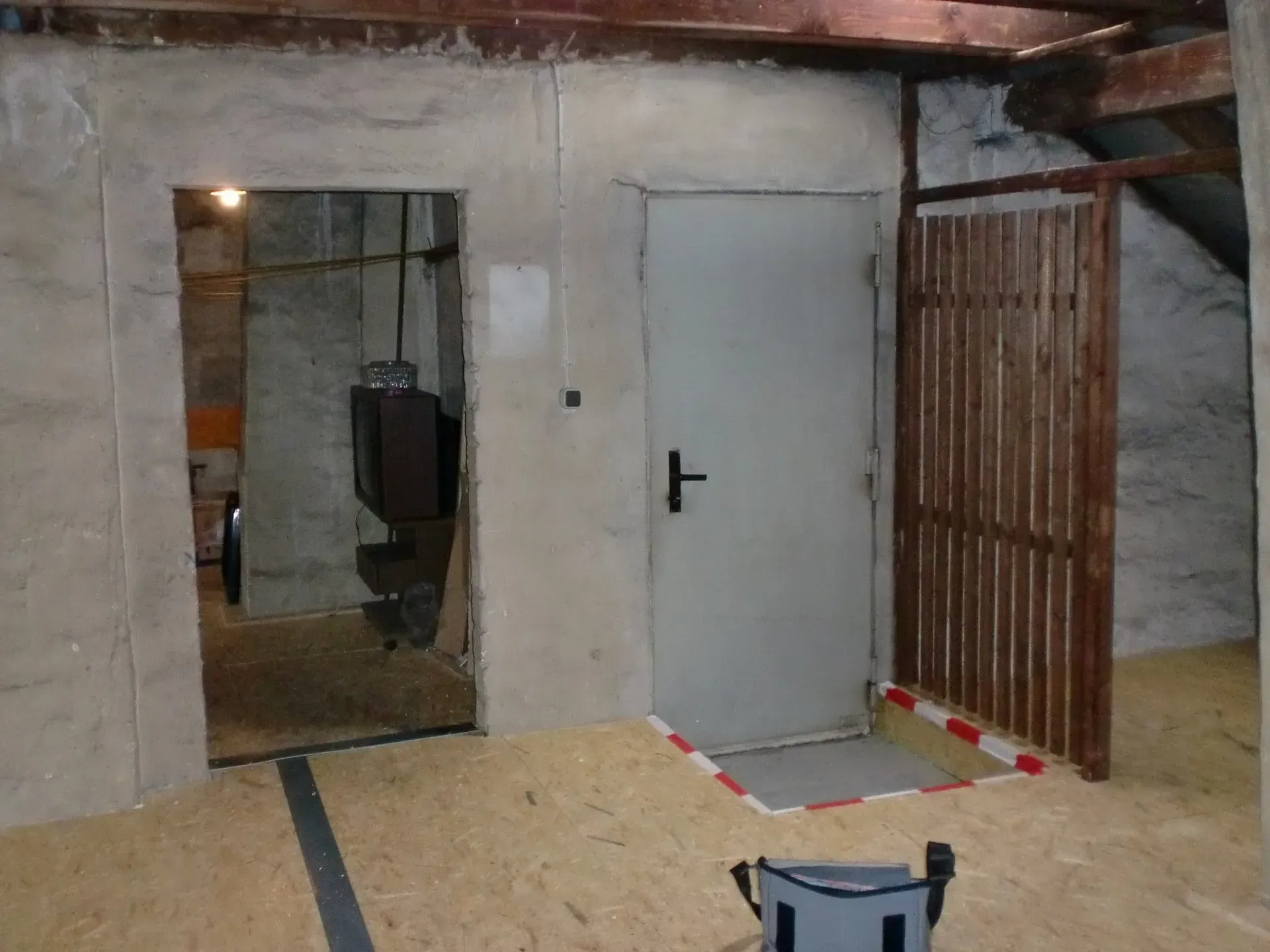 Kellerraum im Bau mit unverputzten Wänden, einer weißen Tür und freiliegenden Holzbalken.