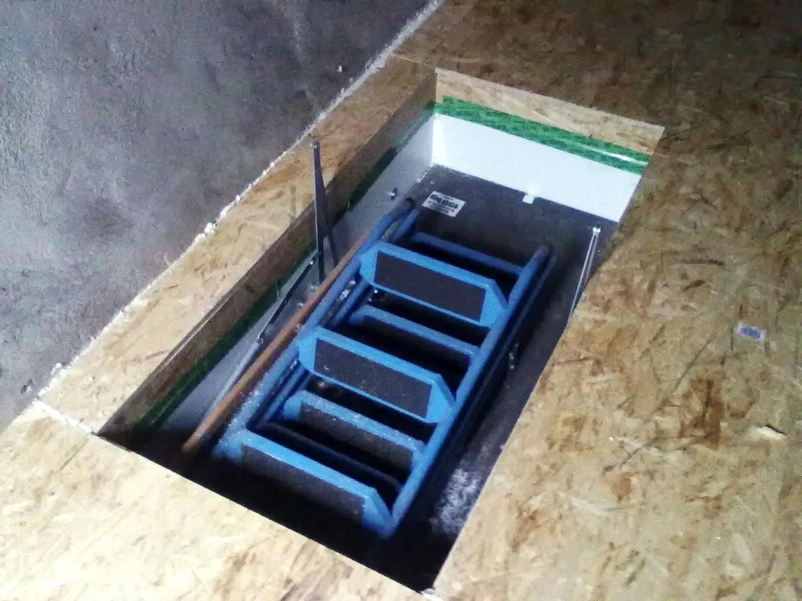Blaue Leiter, die in eine rechteckige Bodenluke hinabführt