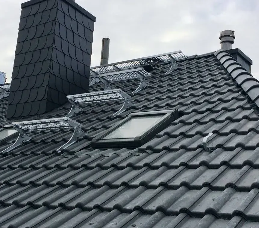 Graues Ziegeldach mit Schornstein, Oberlicht und Schneefanggittern unter einem bedeckten Himmel
