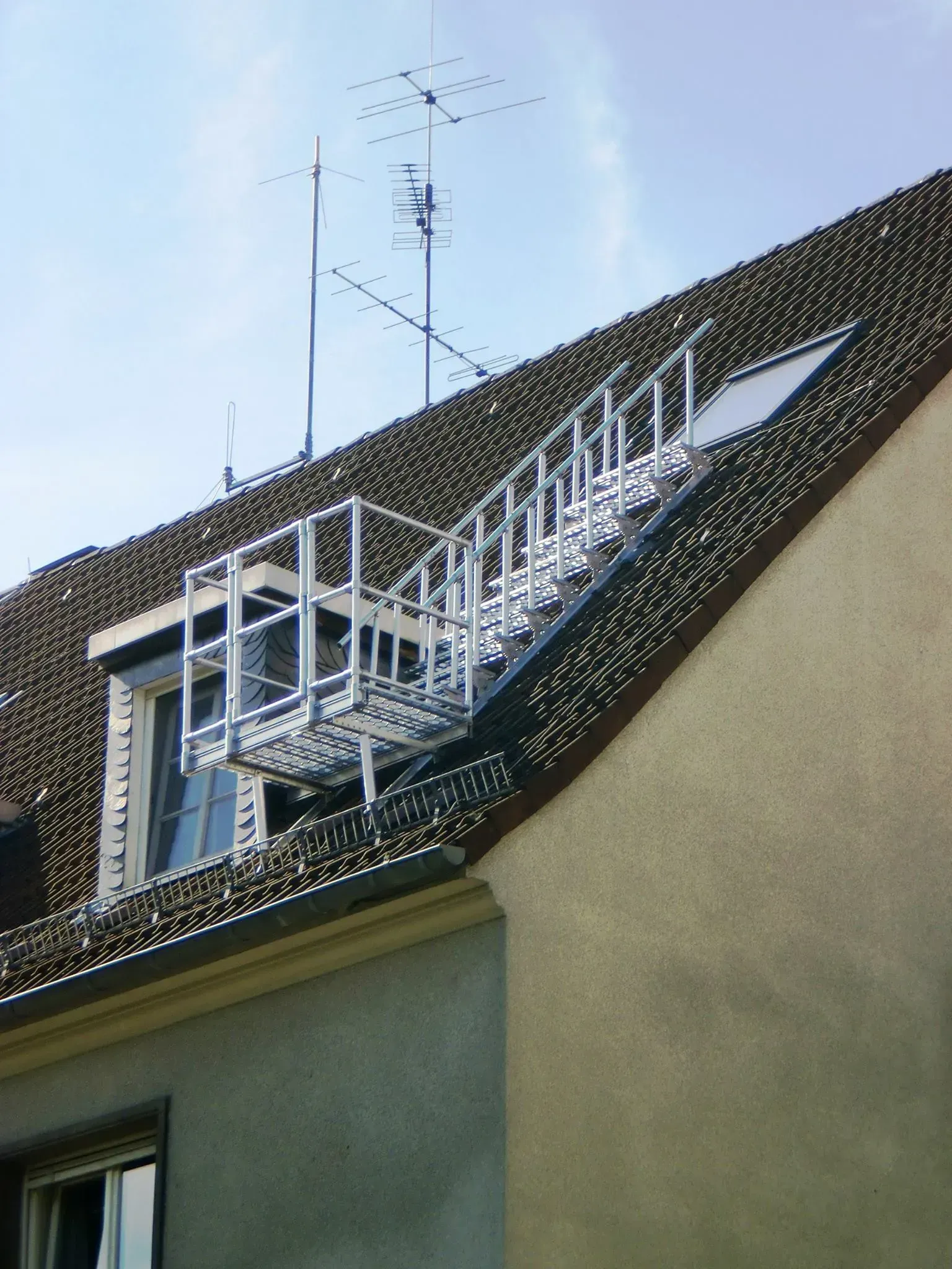 Weiße Metalltreppe oder -steg auf einem schrägen Dach mit einer Antenne über einem Haus.
