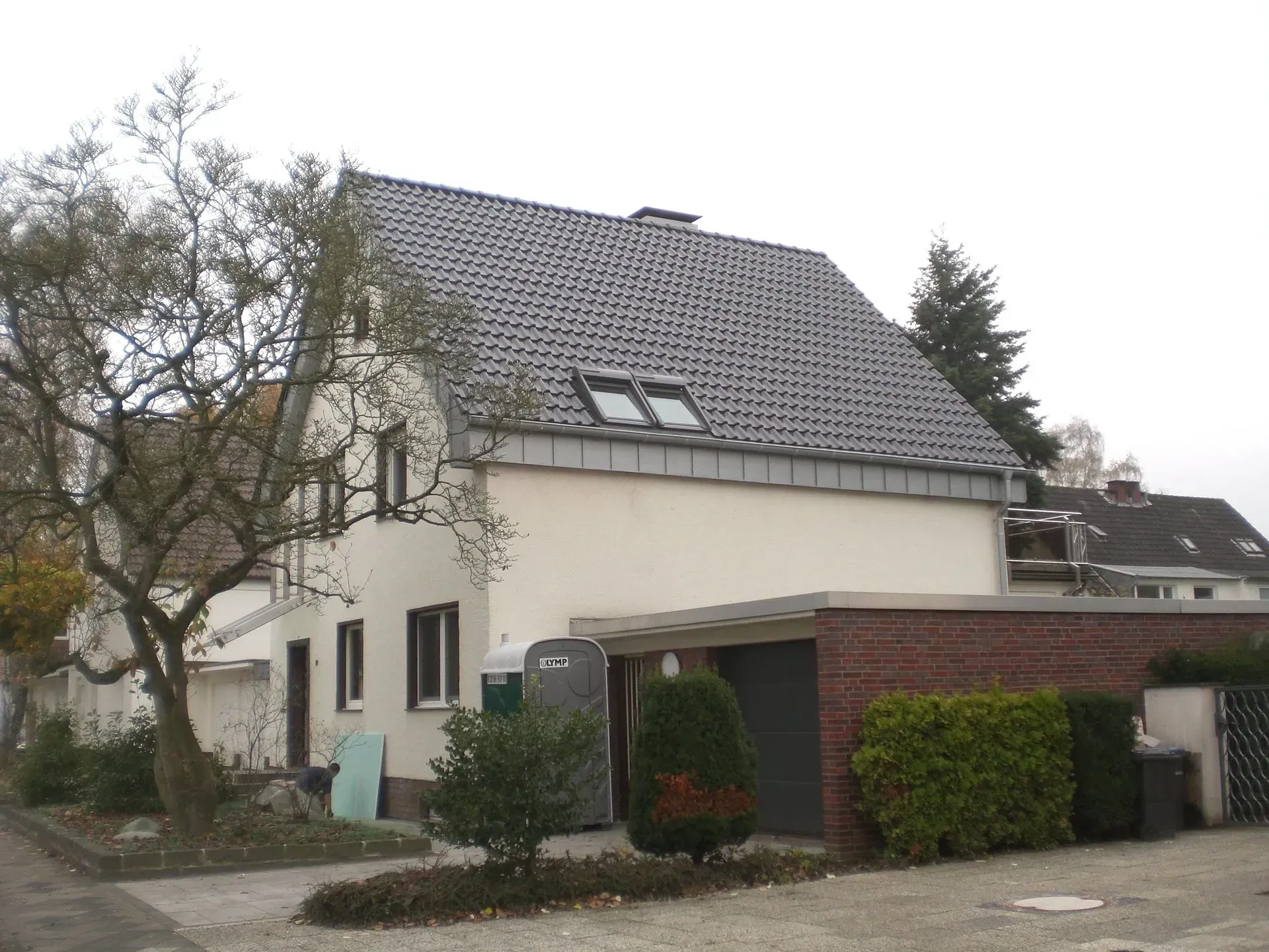 Zweistöckiges Haus mit grauem Ziegeldach, weißen Wänden und einer gemauerten Garage unter einem bedeckten Himmel