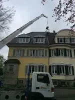 Kranwagen hebt an einem bewölkten Tag Material auf das Dach eines mehrstöckigen Gebäudes.