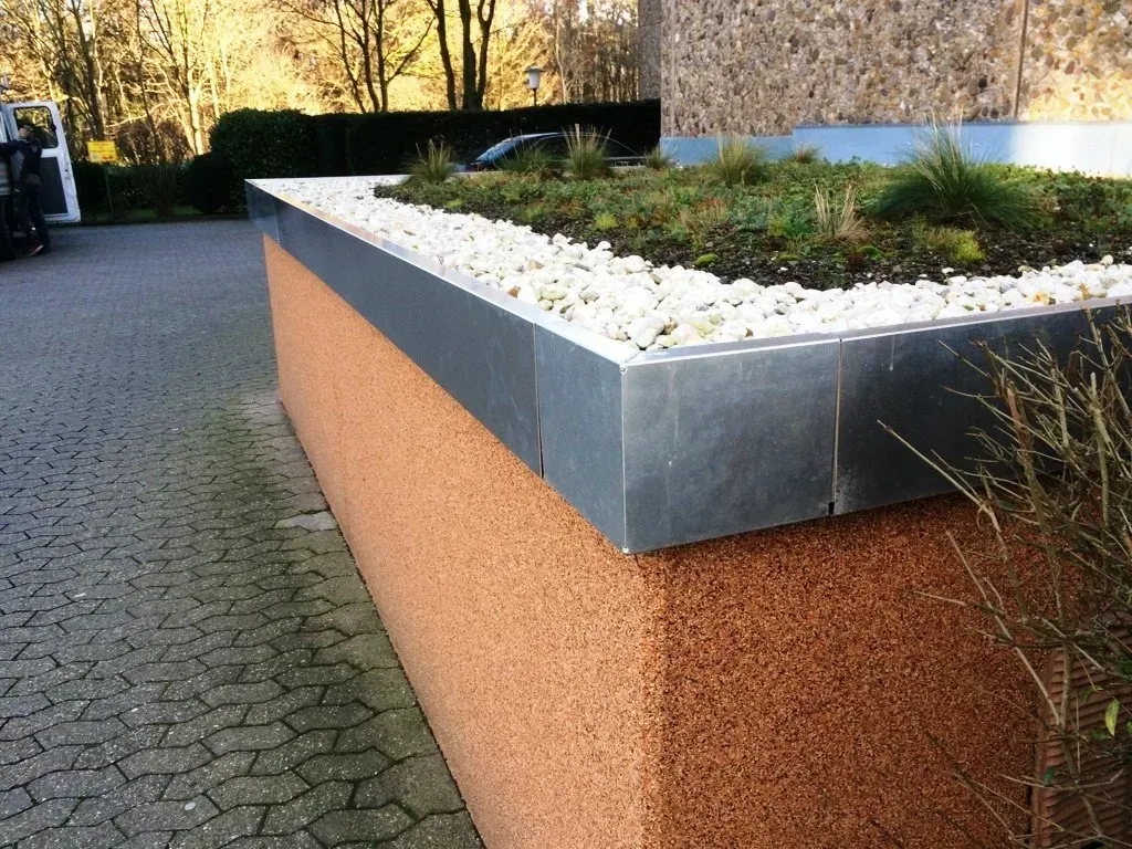 Hochbeet mit grauer Metalleinfassung, weißen Steinen und Grünpflanzen entlang eines gepflasterten Weges