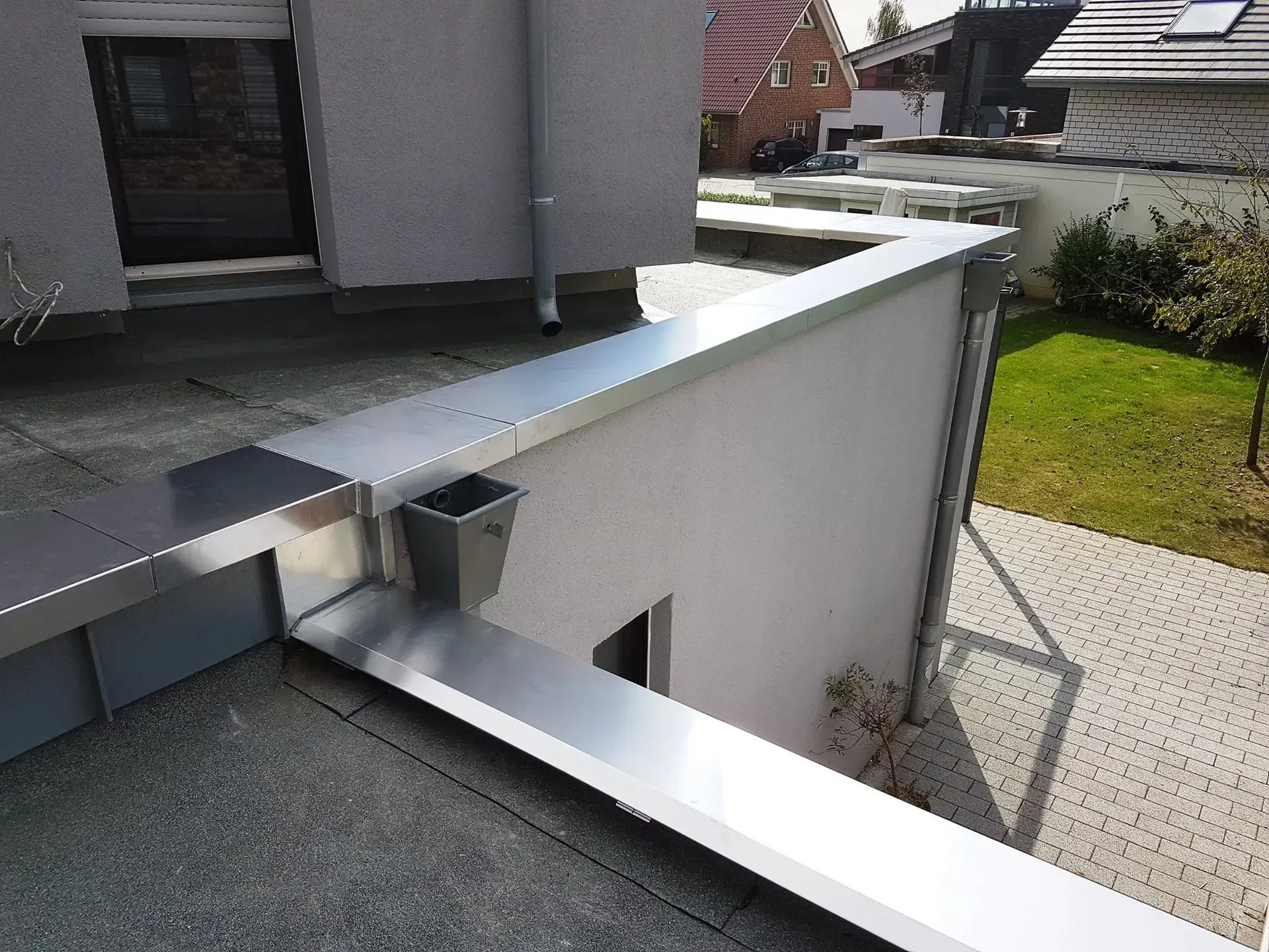 Modernes Hausäußeres mit silbernem Metallgeländer und weißer Mauer neben einem gepflasterten Gehweg
