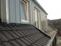 Dunkelgraues Schrägdach mit Dachgauben und darüber eine Reihe heller Fenster.