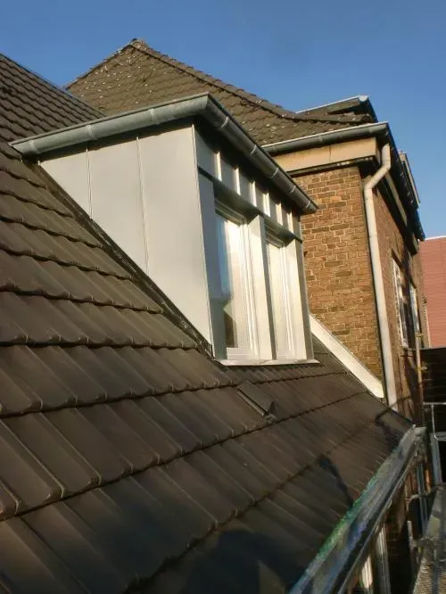 Ein Backsteinhaus mit braunen Ziegeln und einem weißen Dachgaubenfenster im Sonnenlicht