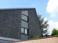 Moderne graue Gebäudefassade mit schmalen vertikalen Fenstern neben einem Baum und blauem Himmel