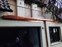 Balkon über einer Garage mit schwarzem Geländer und roter Umrandung an einem beigen Gebäude
