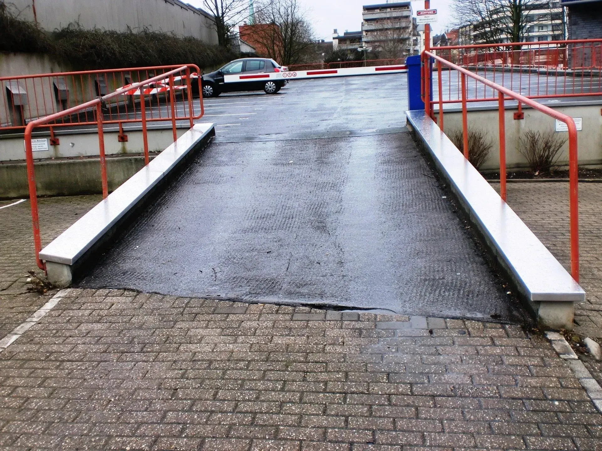 Nasse Rampe mit rotem Geländer führt zu einer Straße in der Nähe von Wohnhäusern