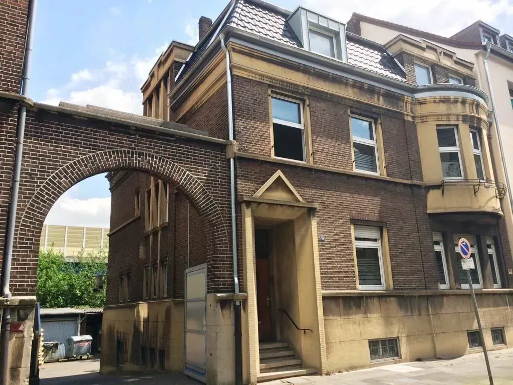 Backsteingebäude mit bogenförmigem, brückenartigem Durchgang und Dachgauben neben einer schmalen Gasse