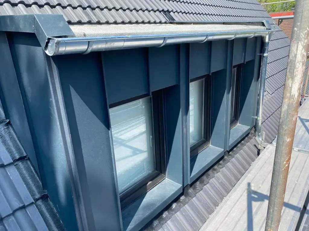 Blaue Dachgauben auf einem grauen Ziegeldach mit Metalldachrinne und Schornsteinrohr