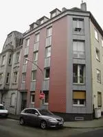 Schmale, rosa-graue Wohnblockwohnung an einer Straßenecke, daneben ein geparktes Auto.