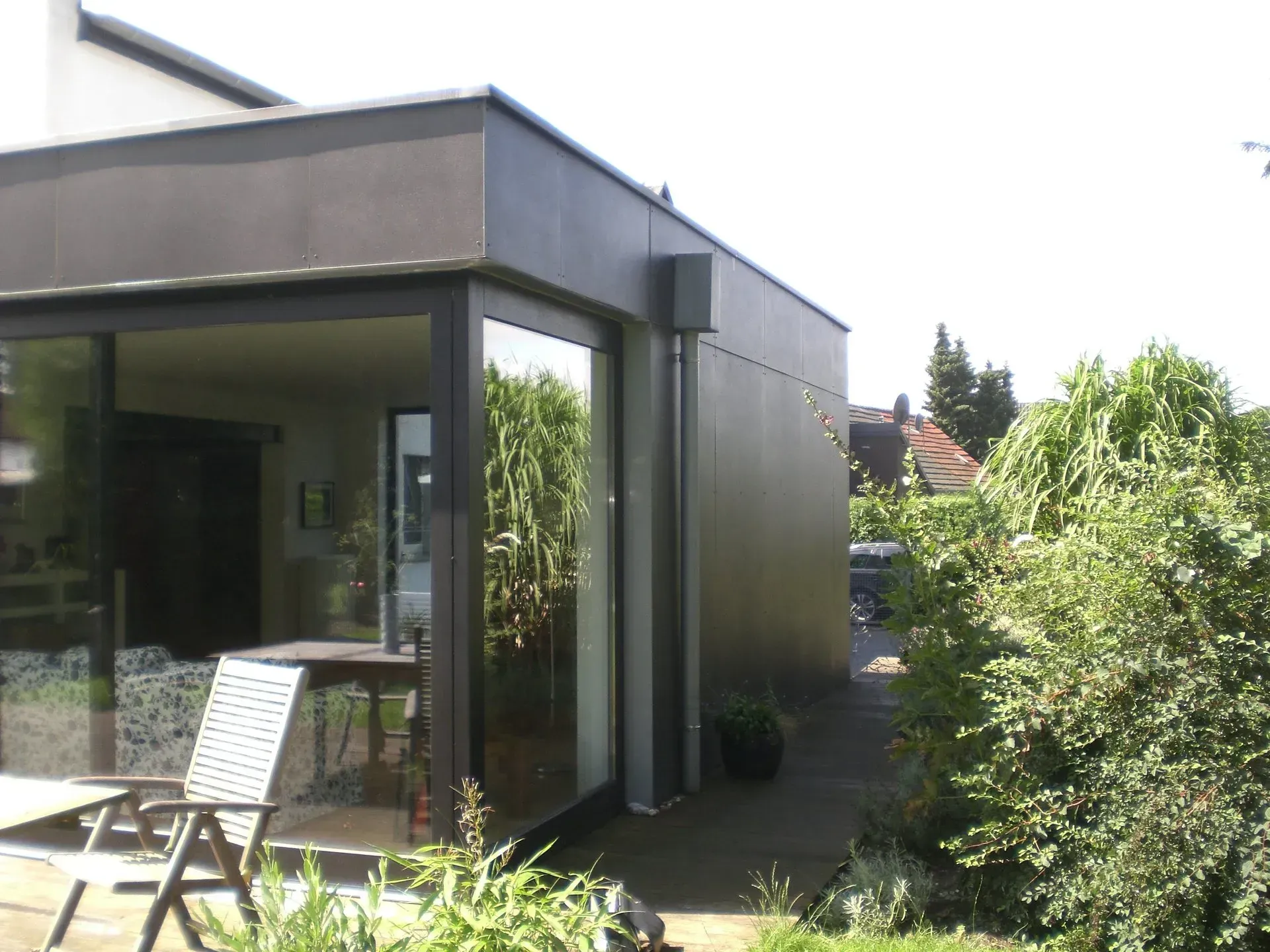 Moderne Hausterrasse mit Glastüren, Liegestuhl und üppigem grünen Garten.