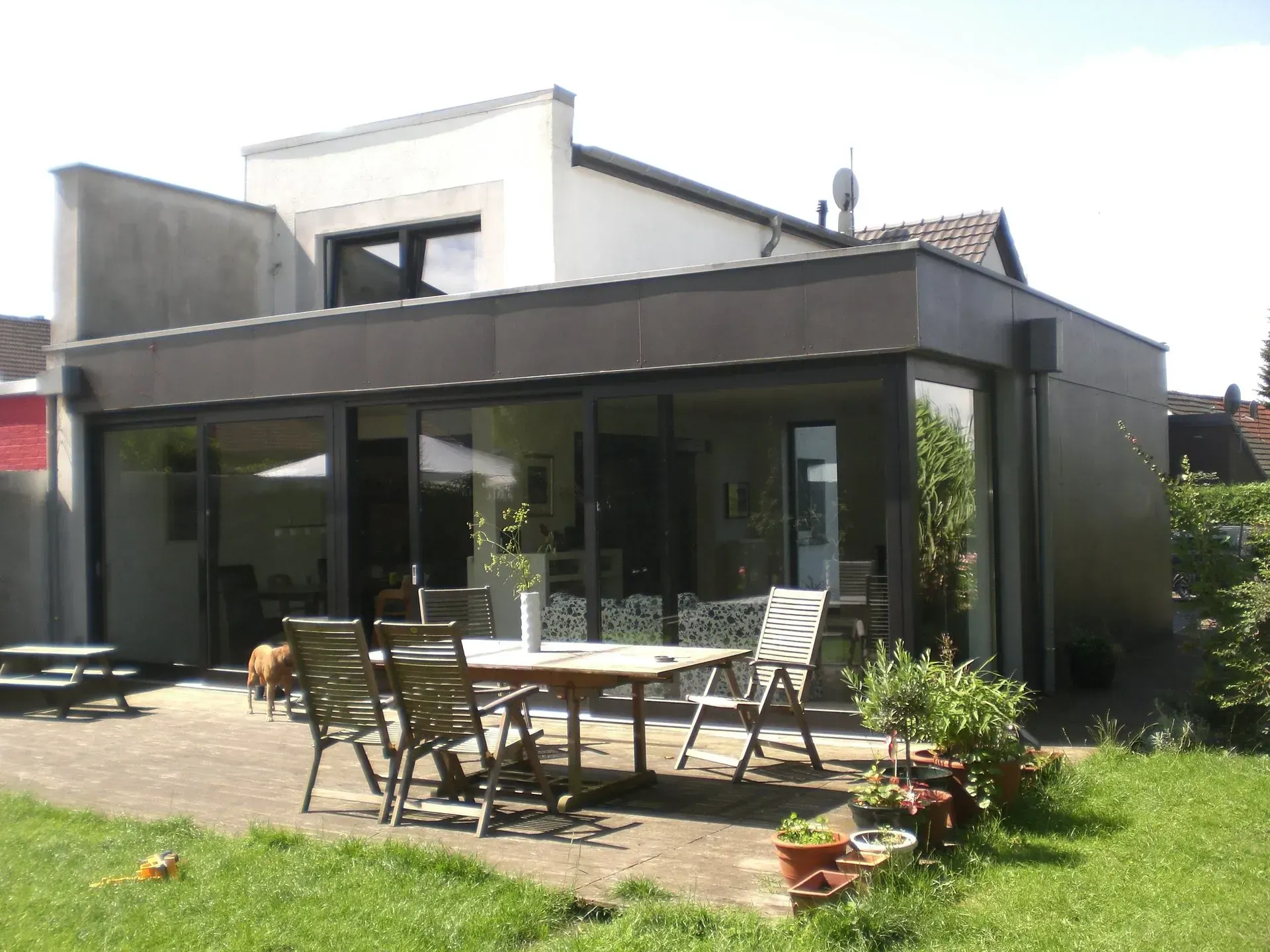 Modernes Haus mit großen Glastüren und einer Terrasse mit Rasenhinterhof.