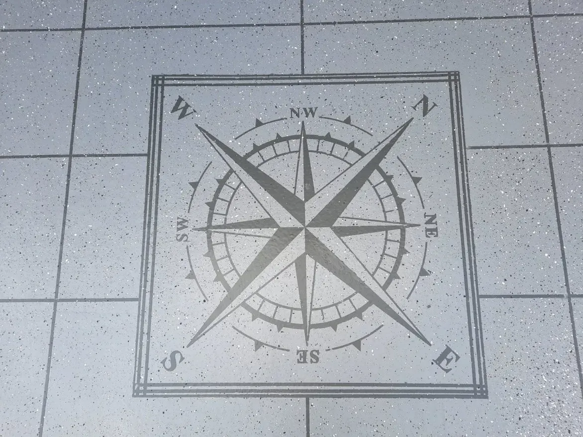 Kompassrosenmotiv auf grauem Fliesenboden, markiert mit den Himmelsrichtungen.