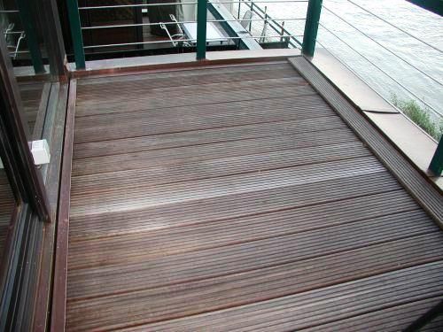Holzterrasse mit integrierter Rampe neben Glasgeländer und gefliestem Gehweg