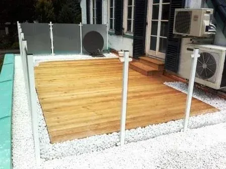 Holzterrasse mit weißen Geländerpfosten und Außenklimaanlagen neben einem Haus