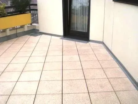Leerer, gefliester Patio mit gelber Bank und Glastüren neben einem Gebäude