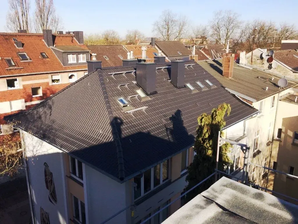 Wohnhausdächer mit Schornsteinen und kahlen Bäumen in einer sonnigen Wohngegend