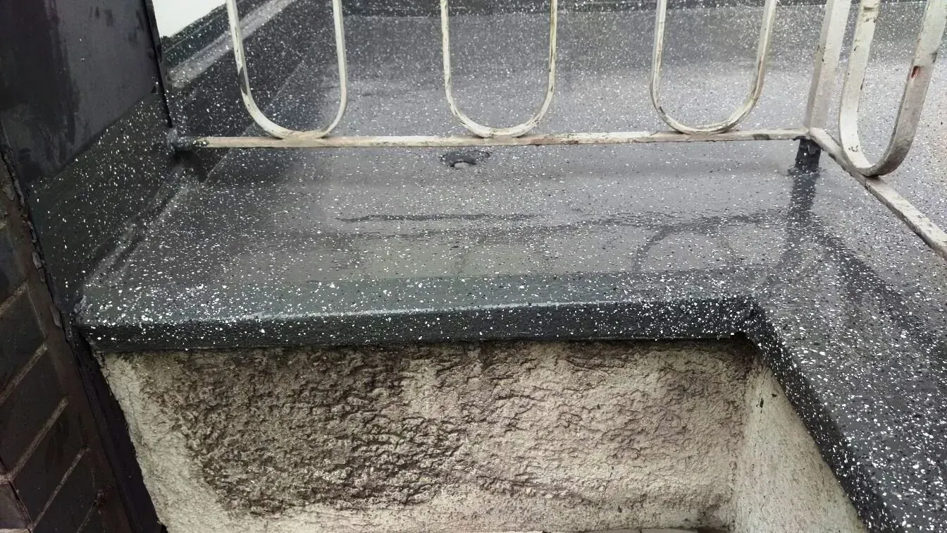 Nahaufnahme einer schwarz gesprenkelten Stufe oder eines Vorsprungs neben einem Metallgeländer und einer Mauer im Freien