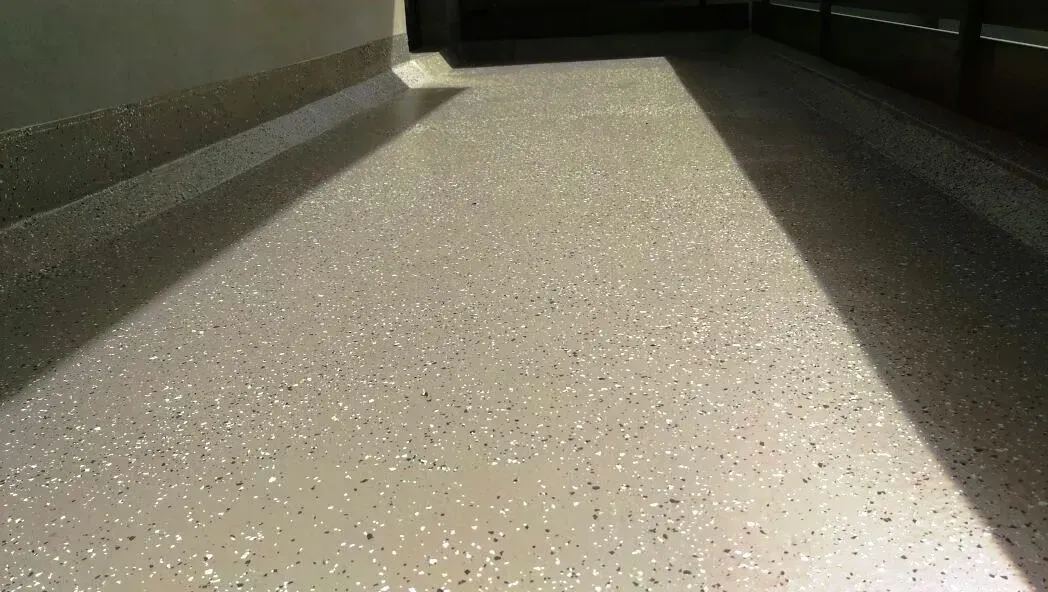 Sonnenbeschienener, gesprenkelter Boden in einem schmalen Flur mit dunklen Wänden und hellem Licht vor uns.