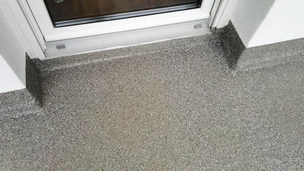 Grau gesprenkelter Boden trifft auf eine Glastürschwelle mit dunkler Eckkante.