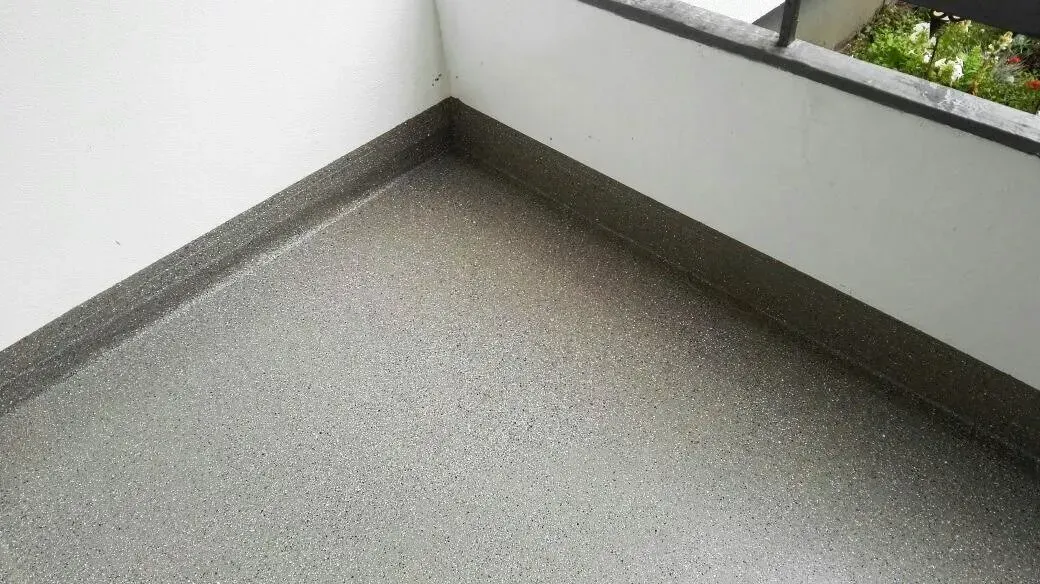 Leere, graue Ecke eines Balkons oder einer Terrasse mit Betonboden und niedriger Mauer.