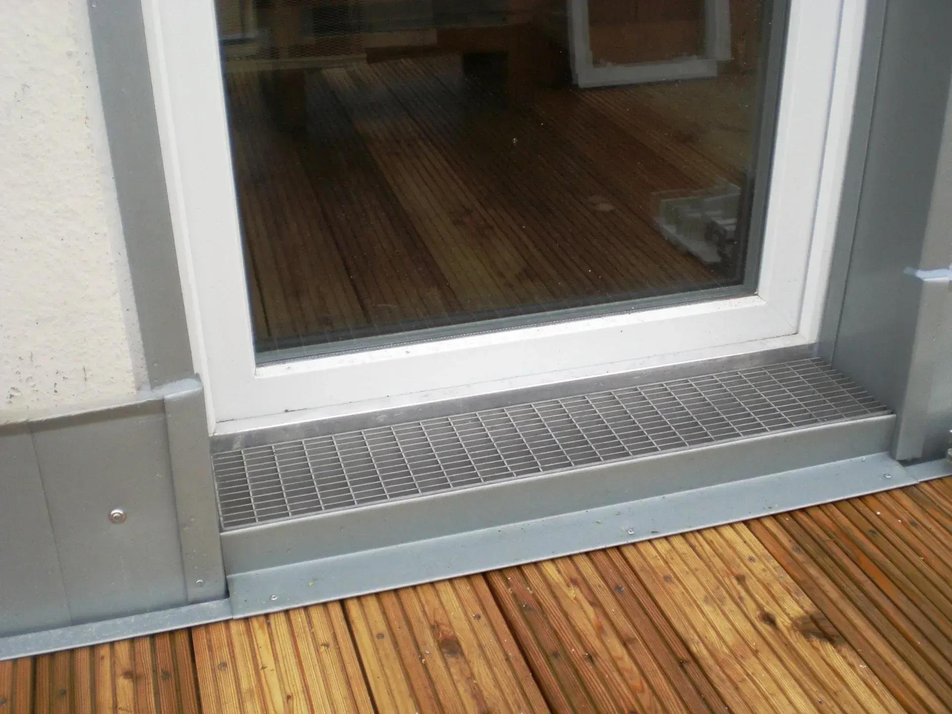 Schiebetür aus Glas mit Metallschwelle und Holzterrasse im Außenbereich