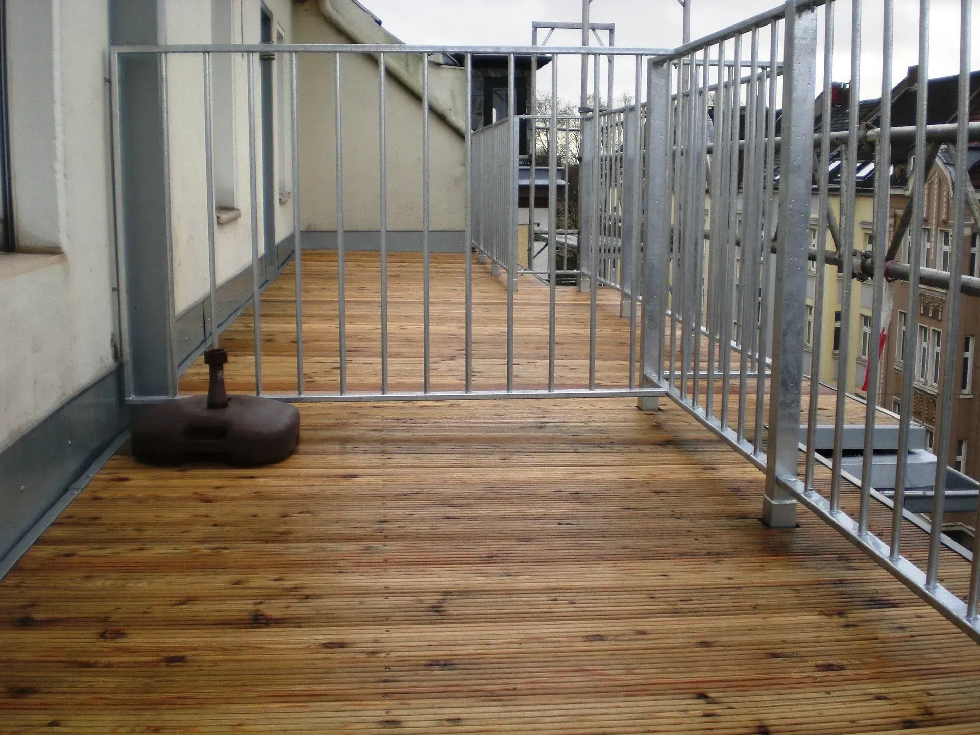 Holzterrasse auf dem Dach mit Metallgeländer und einem dunklen Ottomanen an der Wand