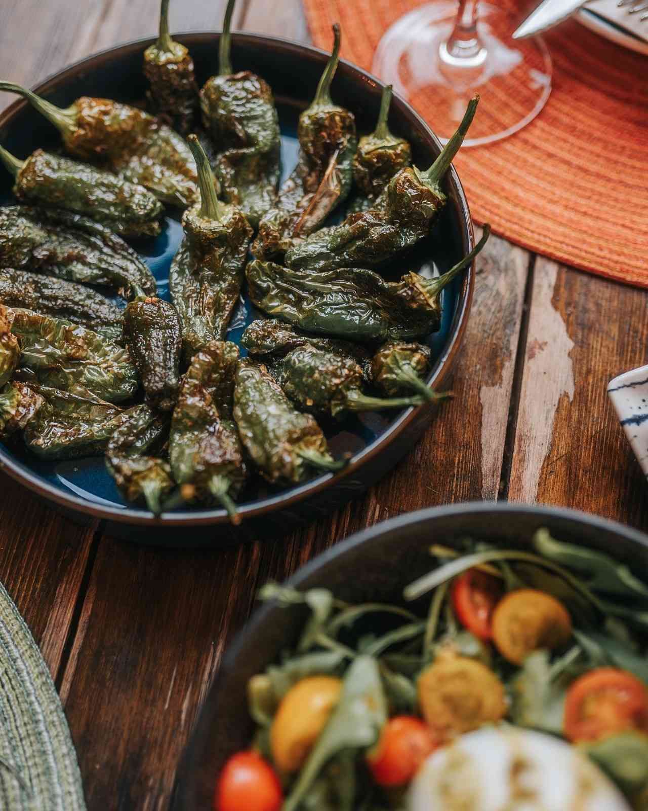 Plato de hojas de parra rellenas sobre una mesa de madera junto a un bol de ensalada y una copa de vino.