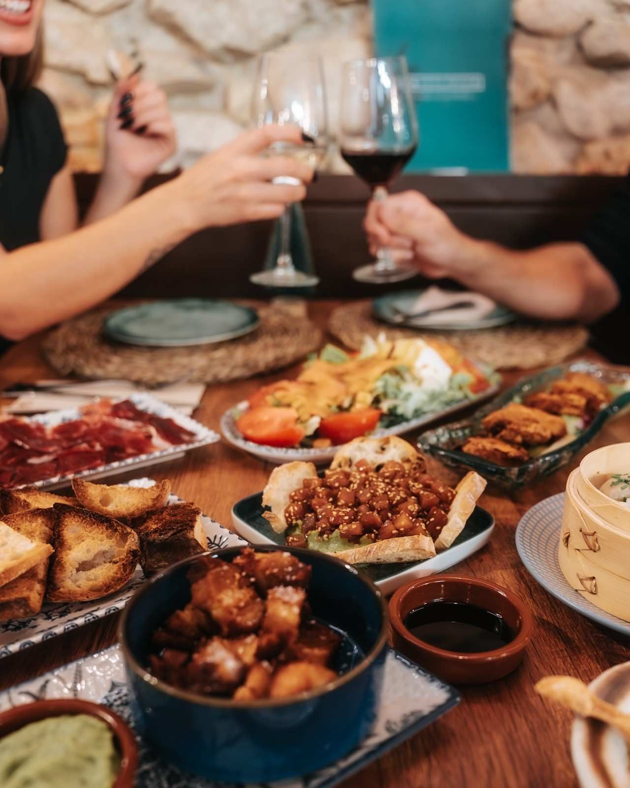 Gente brindando con copas de vino sobre una mesa con platos variados en un restaurante acogedor.
