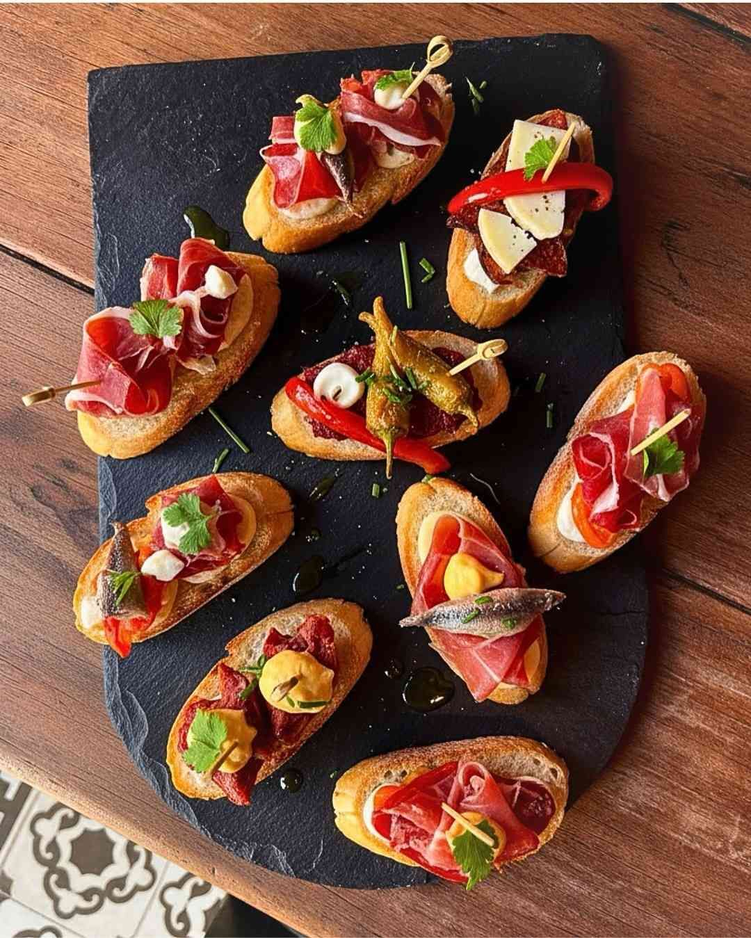 Bruschetta en rodajas cubierta con tomates, hierbas y queso en una tabla de servir negra.