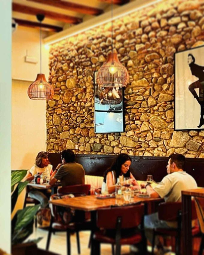 Interior acogedor del restaurante con paredes de piedra y comensales sentados en mesas de madera bajo cálidas luces colgantes.