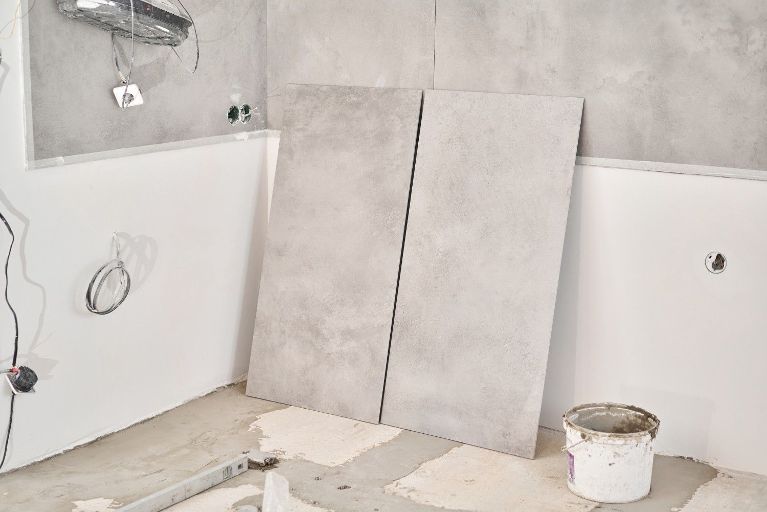 Reforma de baño, con dos grandes azulejos grises apoyados en la pared, paredes blancas y suelo de cemento.