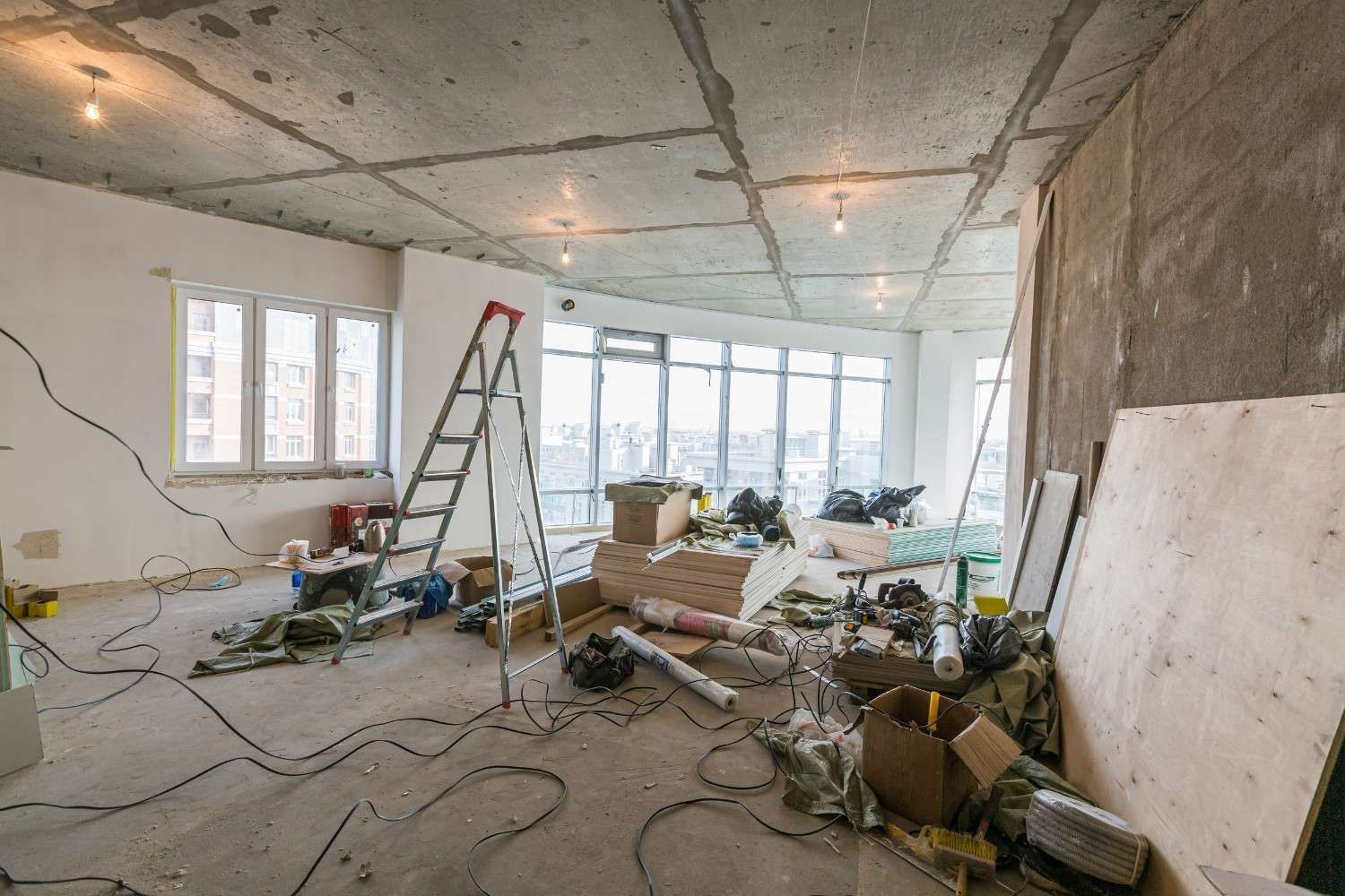 Interior de una habitación en construcción, con cableado, herramientas y materiales de construcción expuestos.