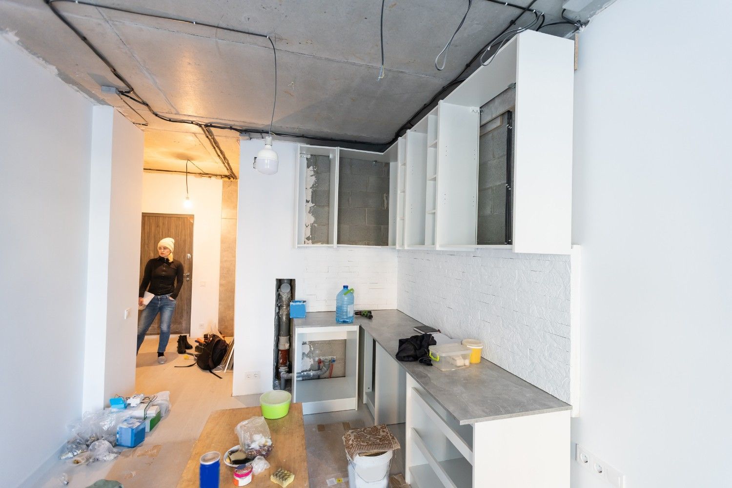 Cocina en construcción, con gabinetes sin terminar, encimera y una persona en la puerta.