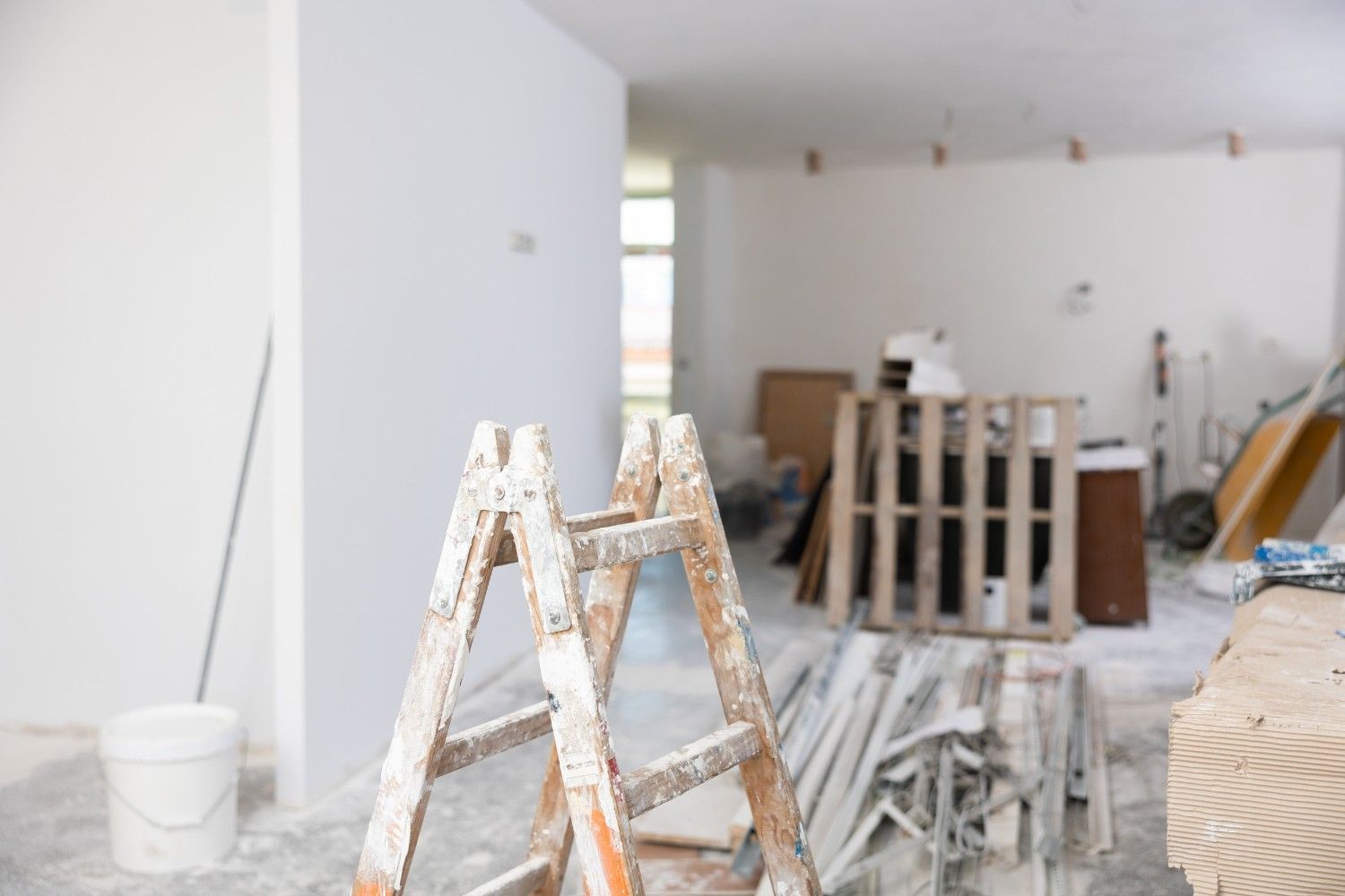 Escalera en una habitación en construcción, paredes blancas, materiales dispersos y un palé.