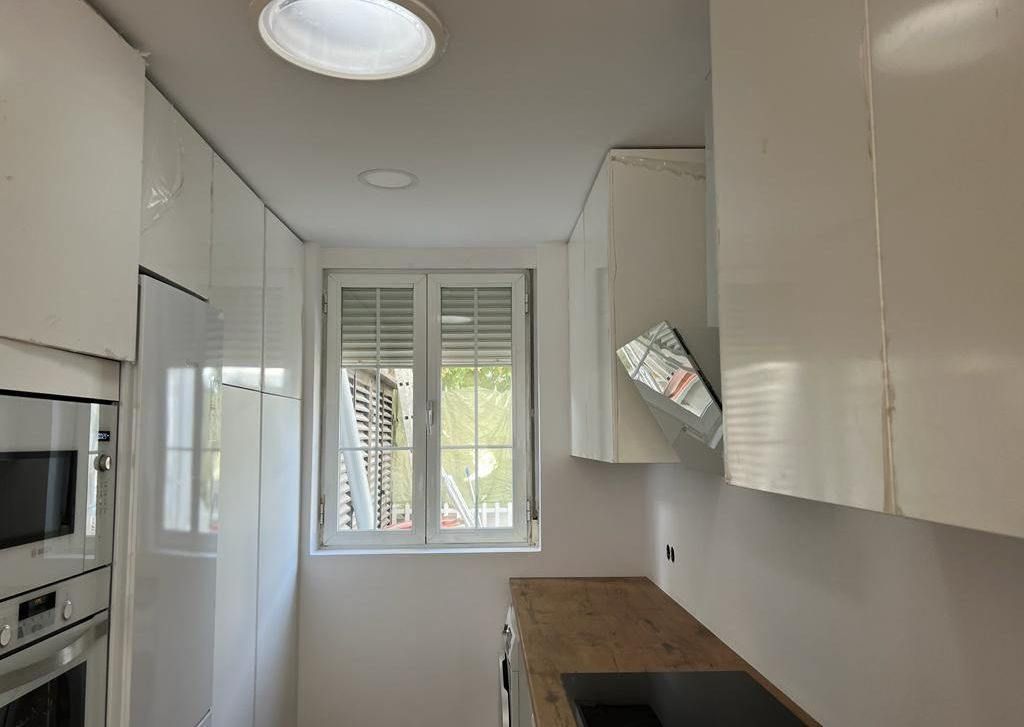 Cocina blanca con gabinetes superiores, ventana y espacio en el mostrador.