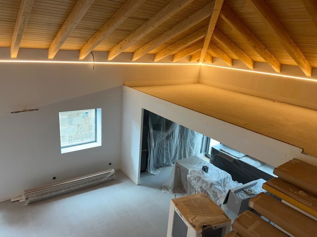 Interior de una habitación con techo de vigas de madera, buhardilla y ventana. Brilla con una luz cálida.