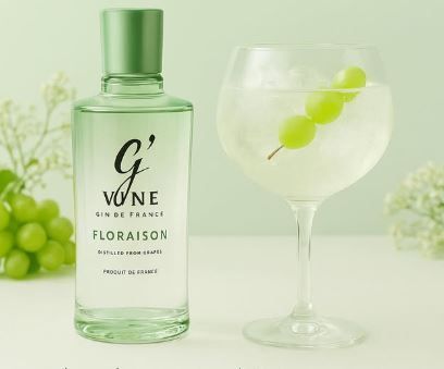 Botella de vino floral Green Vigne junto a una copa con tallo y uvas verde lima sobre un fondo verde pálido.