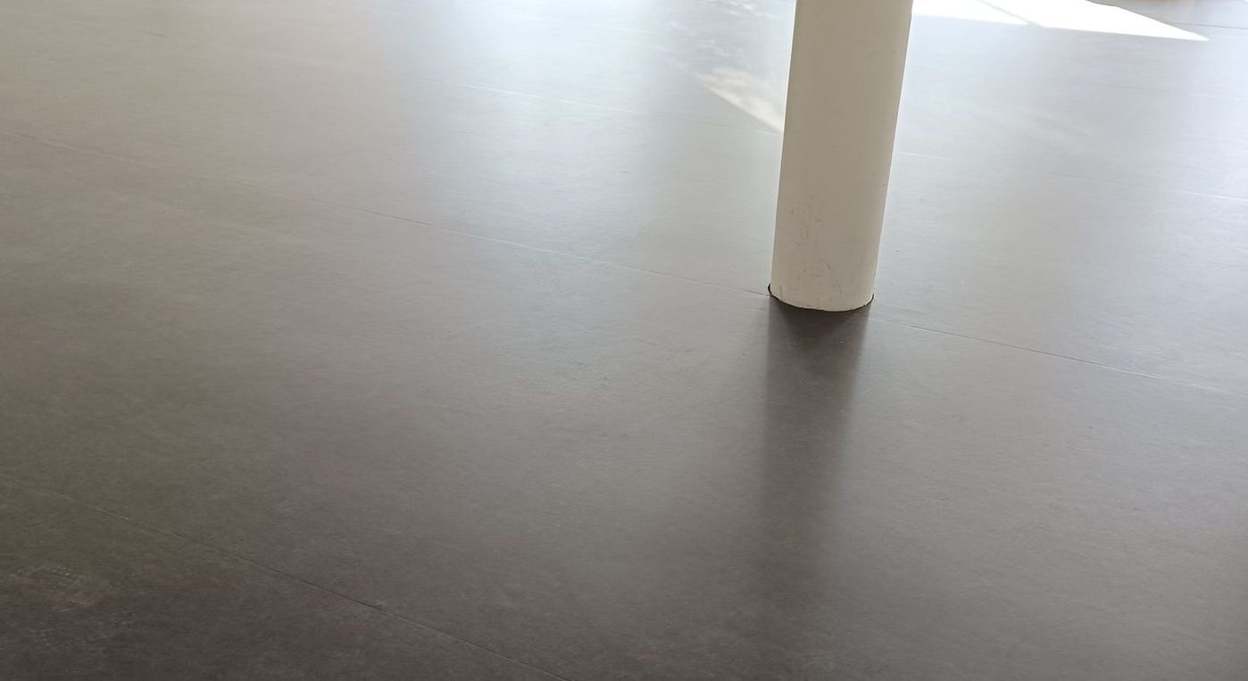 Une personne pose un tapis en caoutchouc noir sur un plancher en bois.