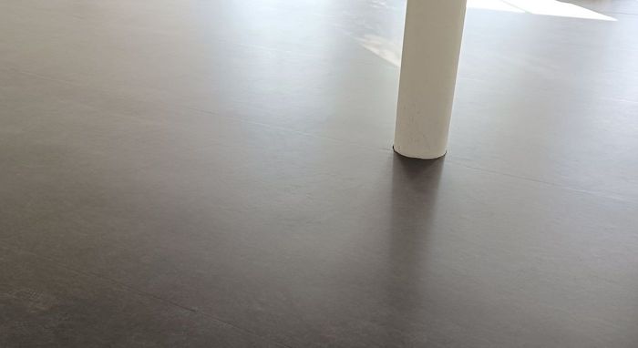 Une personne pose un tapis en caoutchouc noir sur un plancher en bois.