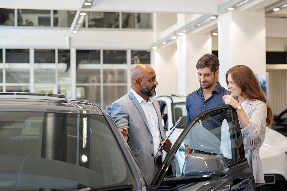 Vendeur conseillant des clients à côté d'une voiture