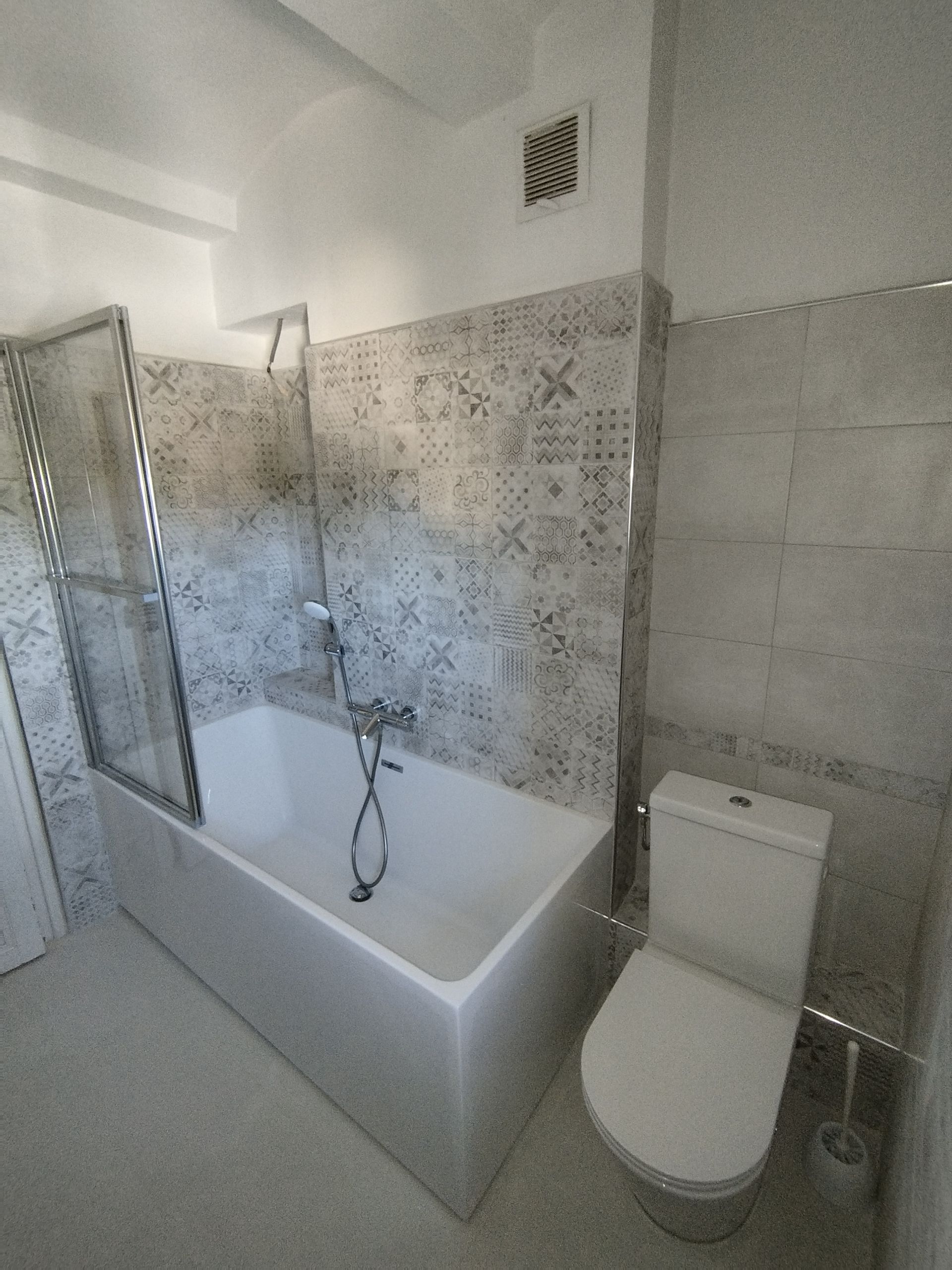 Salle de bains avec une baignoire, les toilettes ; une paroi de douche recouvre la baignoire.