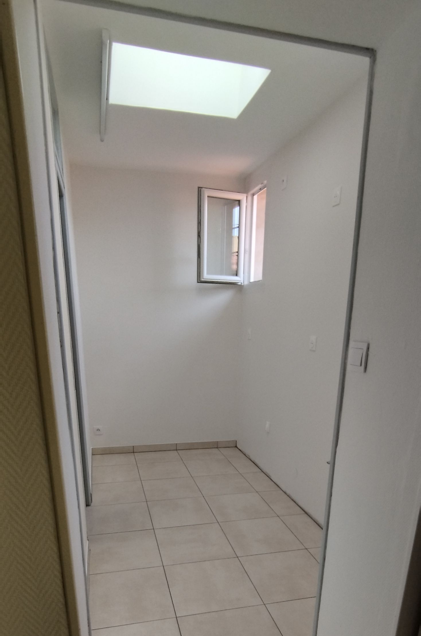 Un sol en carrelage et des murs peints en clair avec une fenêtre et un puits de lumière